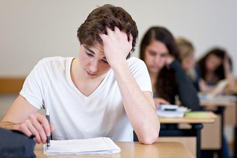 Junger Schüler sitzt über einem Prüfungsbogen in der Schule.